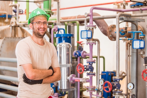 Happy Industry Worker Smiling in Factory Surrounded by Bars and Pipes – Free Download