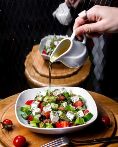 Hand Pouring Olive Oil on Fresh Salad with Feta Cheese, Tomato, and Cucumbers – Free Download