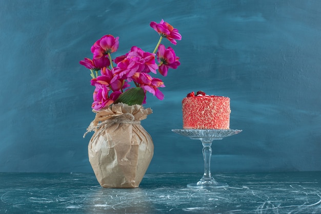 Cake on a Pedestal Beside a Vase of Flowers on a Blue Background – Free Download