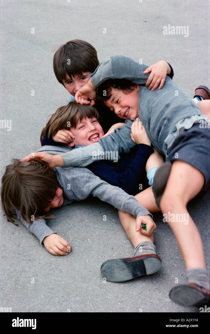 Four school boys outside in playground enjoying play fighting fun Stock